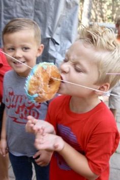 two young boys standing next to each other eating donuts