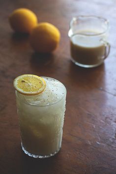 two glasses filled with liquid sitting on top of a wooden table next to oranges