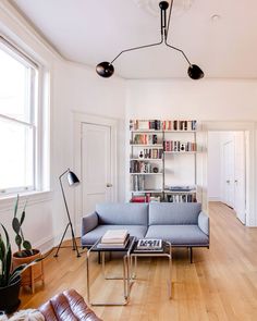 a living room filled with furniture and bookshelves next to a window on top of a hard wood floor