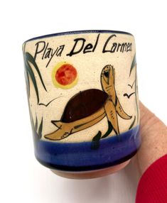 a hand holding a ceramic cup with an image of a turtle on it's side