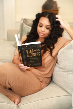 a woman sitting on a couch holding a book in one hand and looking at the camera