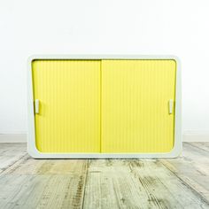 a yellow and white cabinet sitting on top of a wooden floor next to a wall