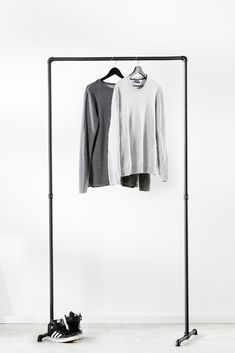 two shirts hanging on a clothes rack next to a pair of black and white shoes