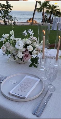 the table is set with white flowers and silverware for an elegant dinner at the beach