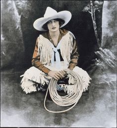 a woman sitting on the ground wearing a cowboy hat and holding a lasso