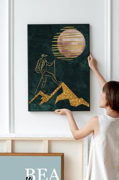 a woman is pointing to a painting on the wall with gold paint and a green background