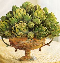 a bunch of artichokes are in a bowl on a tableclothed surface