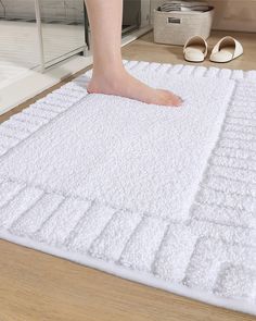 a person standing on top of a white rug in front of a shower door with their feet propped up