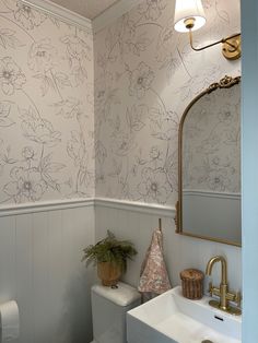 a white toilet sitting next to a sink in a bathroom under a vanity mirror with a gold faucet