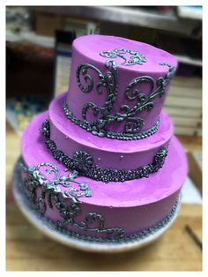 a three tiered cake with purple frosting and silver decorations on it's sides