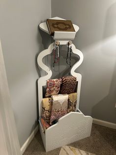 a white shelf with many pillows and jewelry hanging from it's sides in a corner