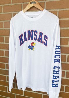 Show off your team pride in this Kansas Jayhawks White Jackson Long Sleeve T Shirt! This KU Jayhawks Long Sleeve Tee features a screen print of team name arched over team logo with team chant on left sleeve. Make sure everyone knows you root for the Jayhawks with this White KU Jayhawks T Shirt. Rock Chalk Jayhawk! Team Chants, Rock Chalk Jayhawk, Ku Jayhawks, Rock Chalk, Kansas Jayhawks, Air Pods, Urban Dresses, Nice Design, Shirt White