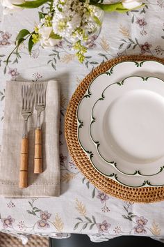 a place setting with white plates and silverware on a floral tableclothed table cloth