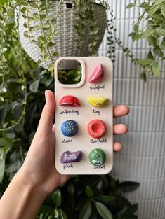 a person holding up a phone case with different colored rocks on it and plants in the background