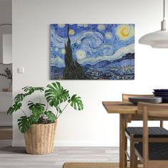 a painting is hanging on the wall above a potted plant in a dining room