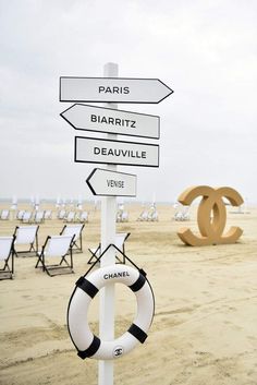 a sign on the beach with chairs in the background