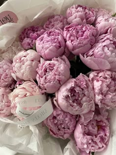 a bouquet of pink peonies is wrapped in white paper and has a name tag