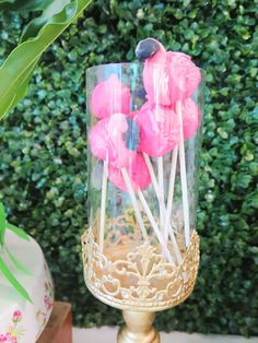 pink and blue lollipops are in a glass container on a table next to a potted plant