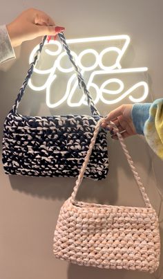 two purses hanging on the wall in front of a neon sign