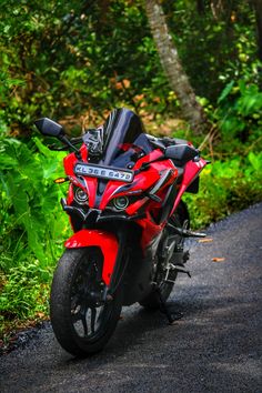 a red motorcycle parked on the side of a road next to lush green trees and bushes