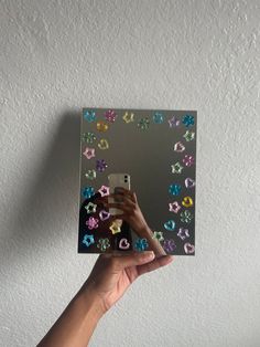 a person holding up a mirror with colorful stickers on it's sides and the reflection of their hand