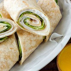 two wraps are sitting on a plate next to a glass of orange juice