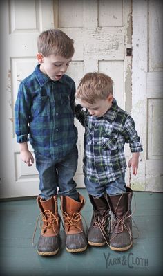 two young boys standing next to each other wearing brown boots and blue plaid shirts with laces on them