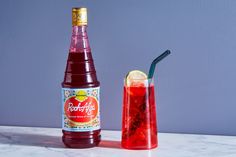 a bottle of booze next to a tall glass with a straw and a lemon slice