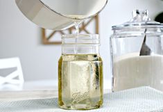 a pitcher pouring milk into a jar on top of a white table cloth next to a glass container