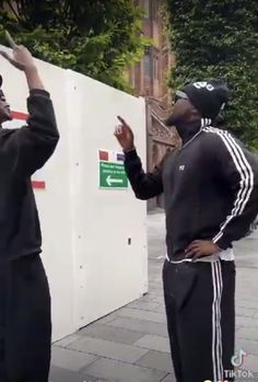 two young men standing next to each other on a sidewalk with their hands in the air