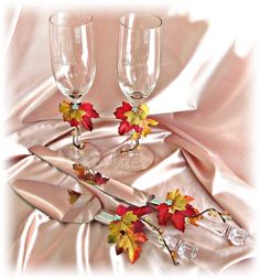 two wine glasses sitting next to each other on a pink satin table cloth with autumn leaves