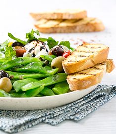 a white plate topped with green beans and toasted bread on top of a table