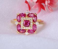 a close up of a pink ring on a white cloth with flowers in the background