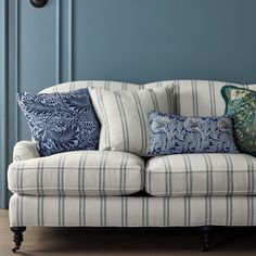 a couch with several pillows on it in front of a blue wall and wooden floor