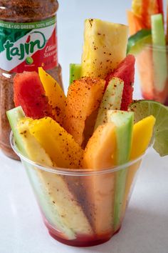 a cup filled with sliced up fruit next to a jar of salt and seasoning