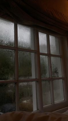 an open window with rain coming down on it and trees in the distance behind it