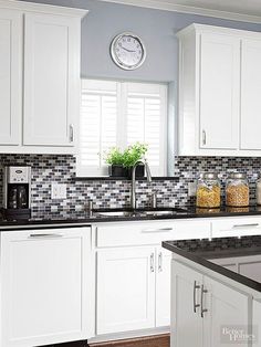 a kitchen with white cabinets and black counter tops is pictured in this image, there is a clock on the wall above the sink