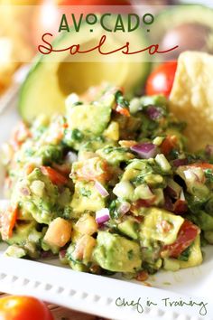 avocado salsa on a white plate with tortilla chips and tomatoes in the background