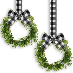 two wreaths hanging from the side of a white wall with black and white checkered ribbon