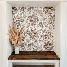 a vase filled with dried flowers sitting on top of a wooden shelf next to a wall