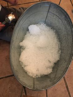 a bucket full of sugar sitting on top of a floor next to a person holding a spoon