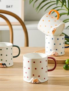 three coffee mugs sitting on top of a wooden table next to a potted plant