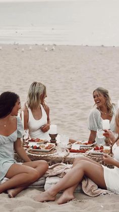 four women sitting on the beach eating food