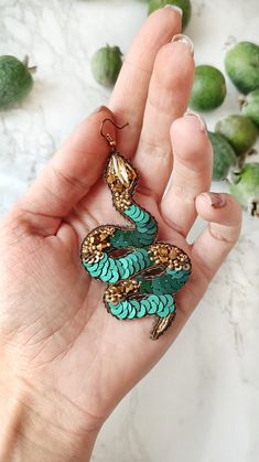 a hand holding a pair of earrings with green beads and gold trimmings on it