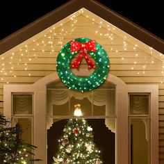 a lighted christmas tree in front of a house with a wreath on it's door