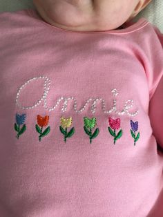 a baby laying on top of a bed wearing a pink t - shirt with flowers