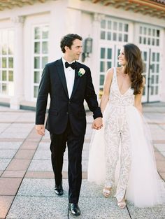 a bride and groom holding hands while walking down the sidewalk in front of a building