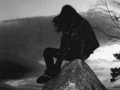 a person sitting on top of a rock next to a tree