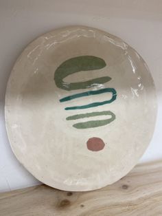 a white plate with green and red designs on it sitting on a wooden table next to a wall