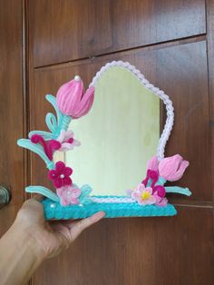 a hand is holding up a mirror with flowers on the front and back sides, in front of a wooden door